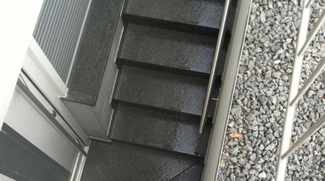 Dunkle, nasse Außentreppe mit Metallgeländer und grauem Kieselsteinboden neben der Treppe, Aufnahme aus der Vogelperspektive.