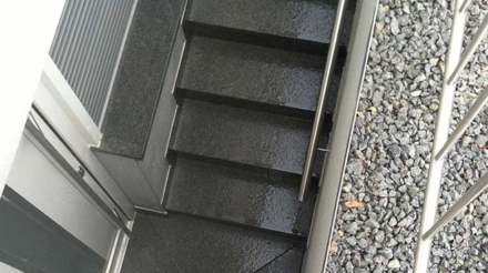 Dunkle, nasse Außentreppe mit Metallgeländer und grauem Kieselsteinboden neben der Treppe, Aufnahme aus der Vogelperspektive.