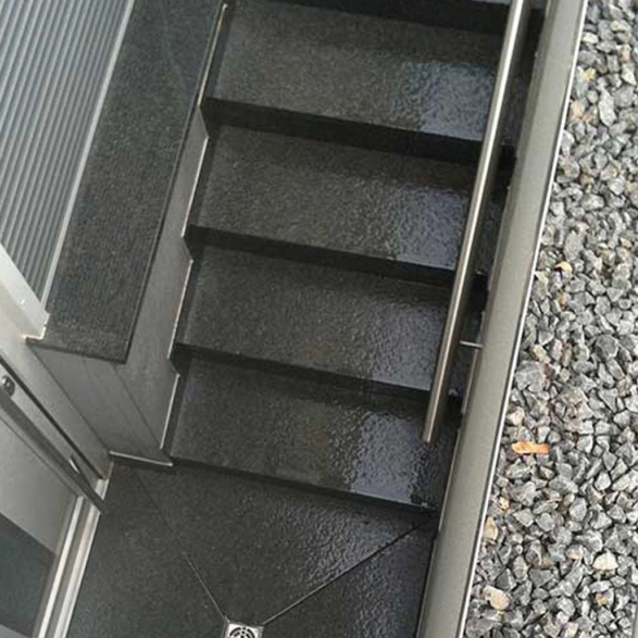 Dunkle, nasse Außentreppe mit Metallgeländer und grauem Kieselsteinboden neben der Treppe, Aufnahme aus der Vogelperspektive.