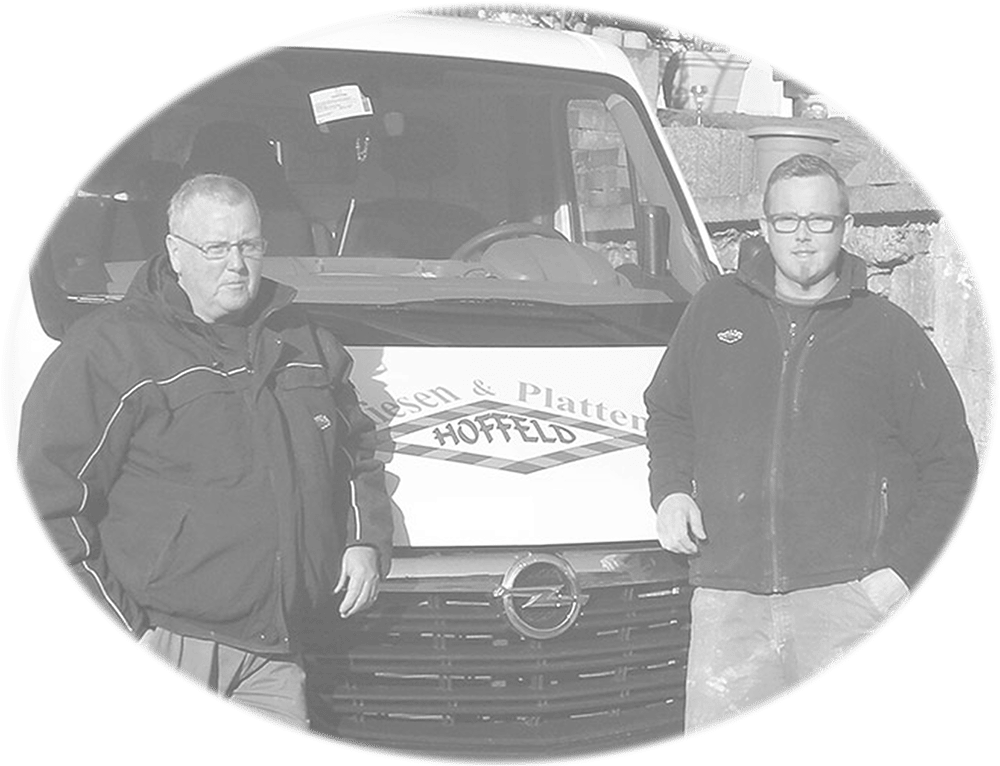 Schwarz-weiß-Bild von zwei Männern in Arbeitskleidung, die vor einem weißen Opel-Transporter mit dem Schriftzug "Fliesen & Platten HOFFELD" lehnen, mit einer Steinmauer im Hintergrund.